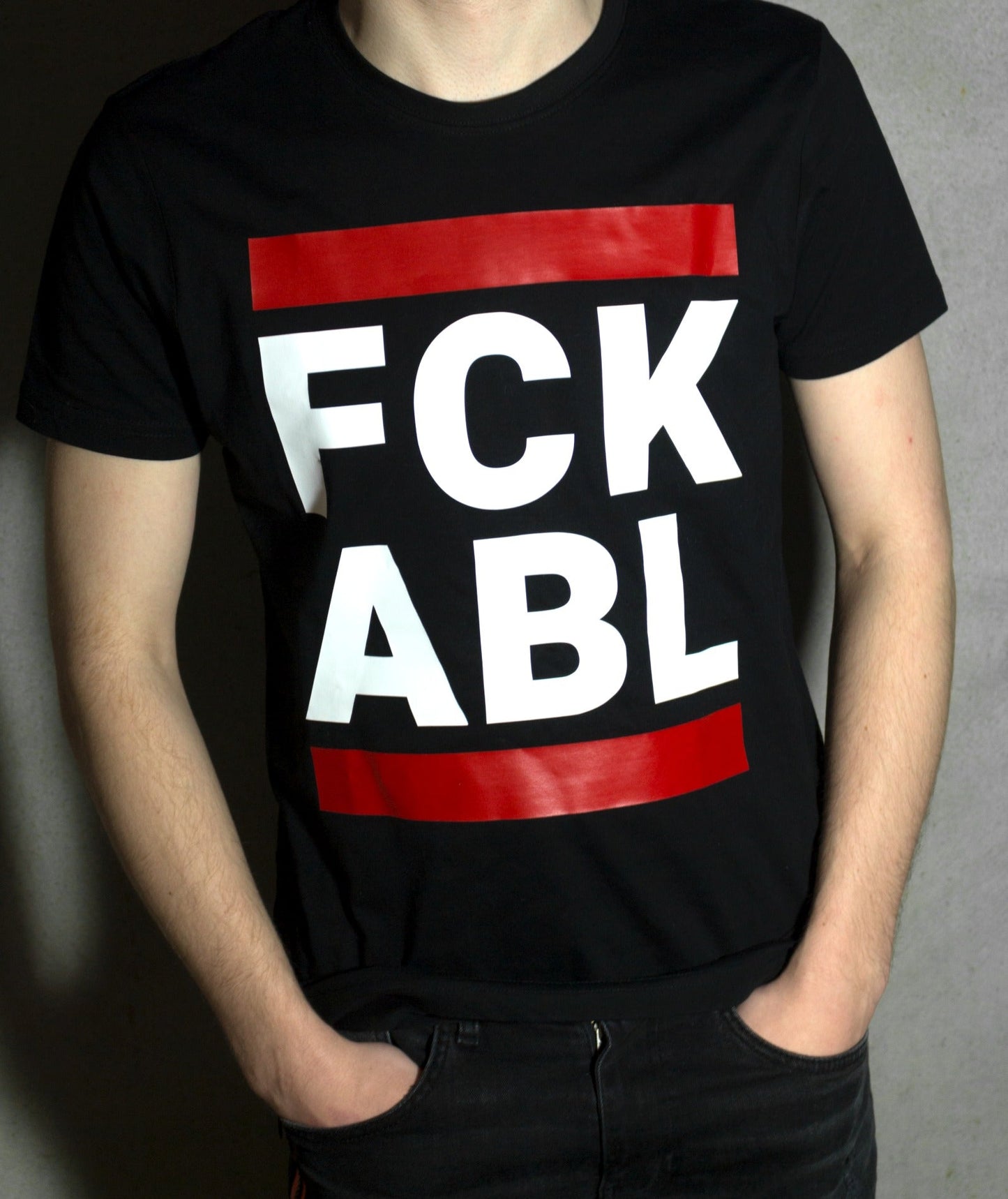 junge vor einer wand mit einem schwarzen t-shirt und dem aufdruck fck abl in weiss und zwei roten blaken
