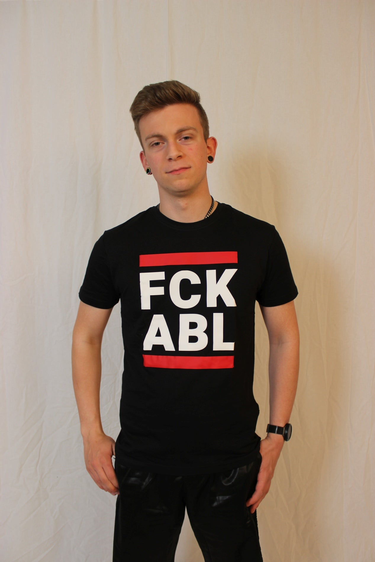 junge vor einer wand mit einem schwarzen t-shirt und dem aufdruck fck abl in weiss und zwei roten blaken
