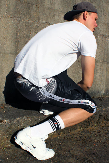 sk8erboy shiny glaenzend satin silver silber glanz boxershort brief mit fettem sk8erboy streifen in weiss mit schwarzem Schriftzug und roter acht 8 seine sexy behaarten beine enden in geilen nike Shox nz sneaker sneax von nike weiss Leder perfekt zu lecken die deluxe socks in weiss von sk8erboy mit schwarzen ringen runden das perfekt ab das logo ist gestickt mit einer roten acht der boy Bengel Kerl mann steht vor einer Backsteinwand an einem roten lostplace Fabrik weg beton geiler blick