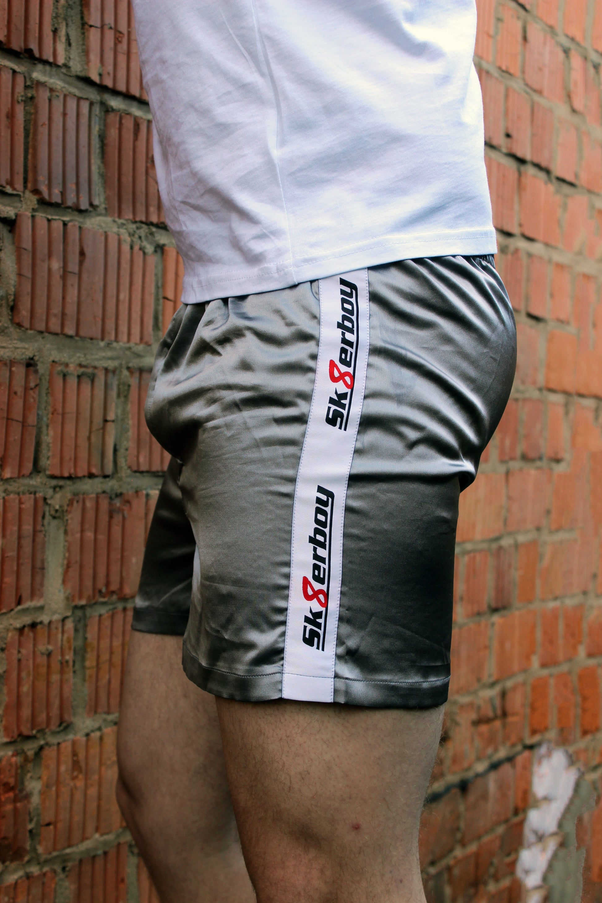 sk8erboy shiny glaenzend satin silver silber glanz boxershort brief mit fettem sk8erboy streifen in weiss mit schwarzem Schriftzug und roter acht 8 seine sexy behaarten beine enden in geilen nike Shox nz sneaker sneax von nike weiss Leder perfekt zu lecken die deluxe socks in weiss von sk8erboy mit schwarzen ringen runden das perfekt ab das logo ist gestickt mit einer roten acht der boy Bengel Kerl mann steht vor einer Backsteinwand an einem roten lostplace Fabrik weg beton fette beule