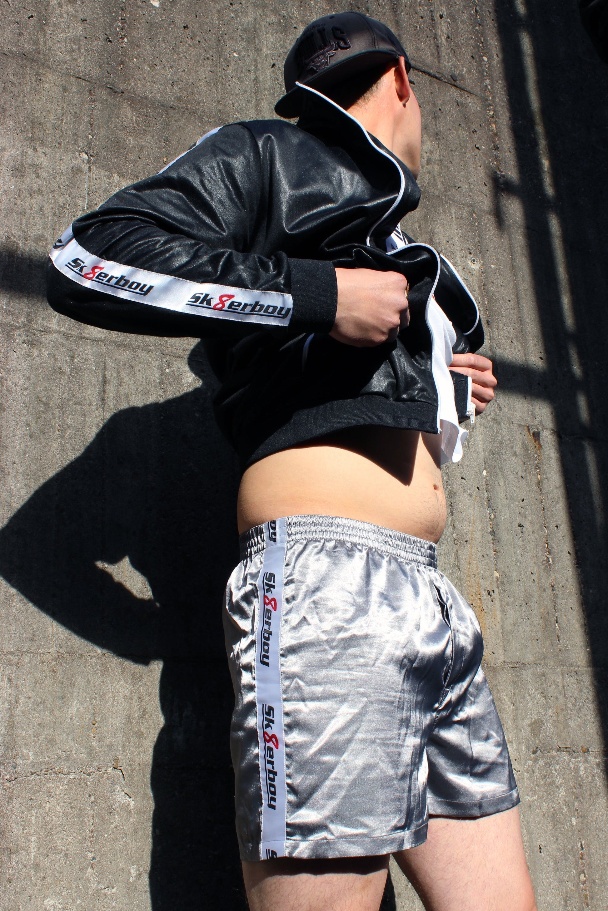 sk8erboy shiny glaenzend satin silver silber glanz boxershort brief mit fettem sk8erboy streifen in weiss mit schwarzem Schriftzug und roter acht 8 seine sexy behaarten beine enden in geilen nike Shox nz sneaker sneax von nike weiss Leder perfekt zu lecken die deluxe socks in weiss von sk8erboy mit schwarzen ringen runden das perfekt ab das logo ist gestickt mit einer roten acht der boy Bengel Kerl mann steht vor einer Backsteinwand an einem roten lostplace Fabrik weg beton Jacke wird hochgezogen