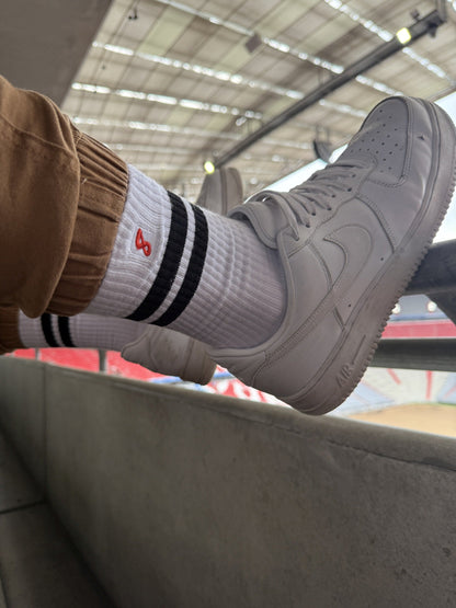 Nahaufnahme von Sk8erboy® Retro Socken mit schwarzen Streifen, getragen mit weißen Nike-Sneakern im Stadion – sportlicher Gay-Look mit Statement-Faktor.