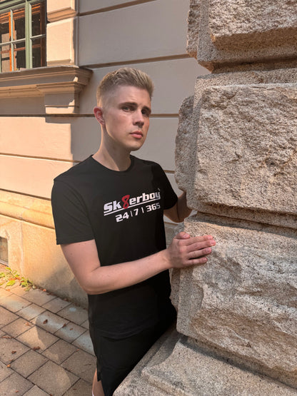 hübscher gay twink trägt ein sk8erboy t-shirt shirt in schwarz baumwolle cotton mit einem sk8erboy aufdruck mit weisser schrift und 8 acht in rot mit 24 7 365 fetter aufdruck