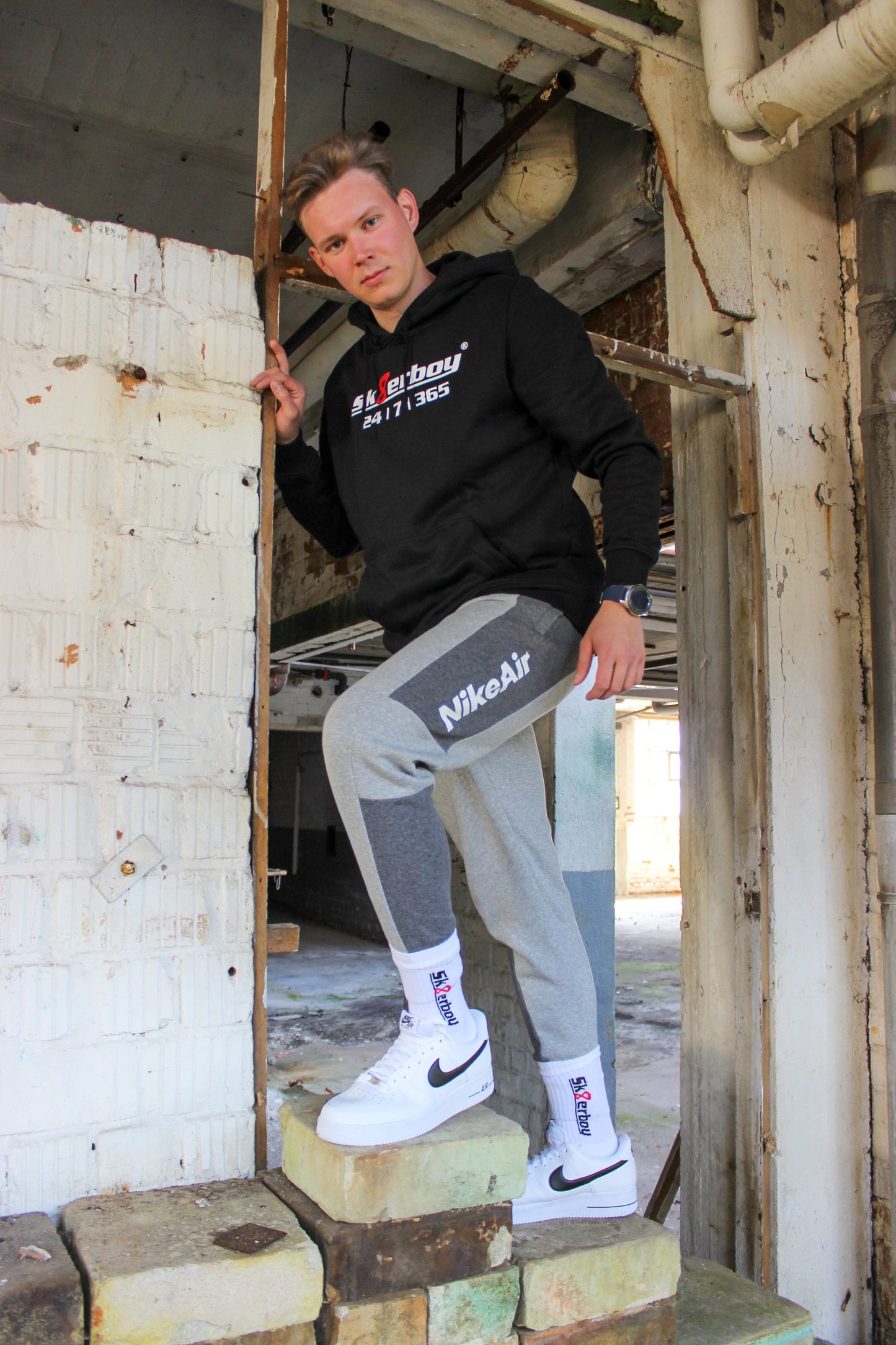 sk8erboy crew socken socks in weiss mit schwarzem schriftzug und roter acht 8 er traegt rot weiss schwarz nike tn tuned 3 drei III er traegt eine graue sweatpant von nike im hintergrund ein lost place farbik