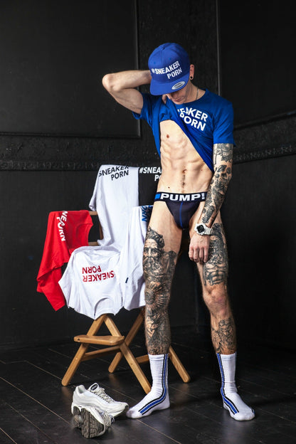 scharfer junge mit jock von pump! zeigt seine tattoos und trägt ein blaues t-shirt und kappe mit sneakerporn aufdruck und den passenden socken in weiss und royalblau mit #sneakerporn von sk8erboy