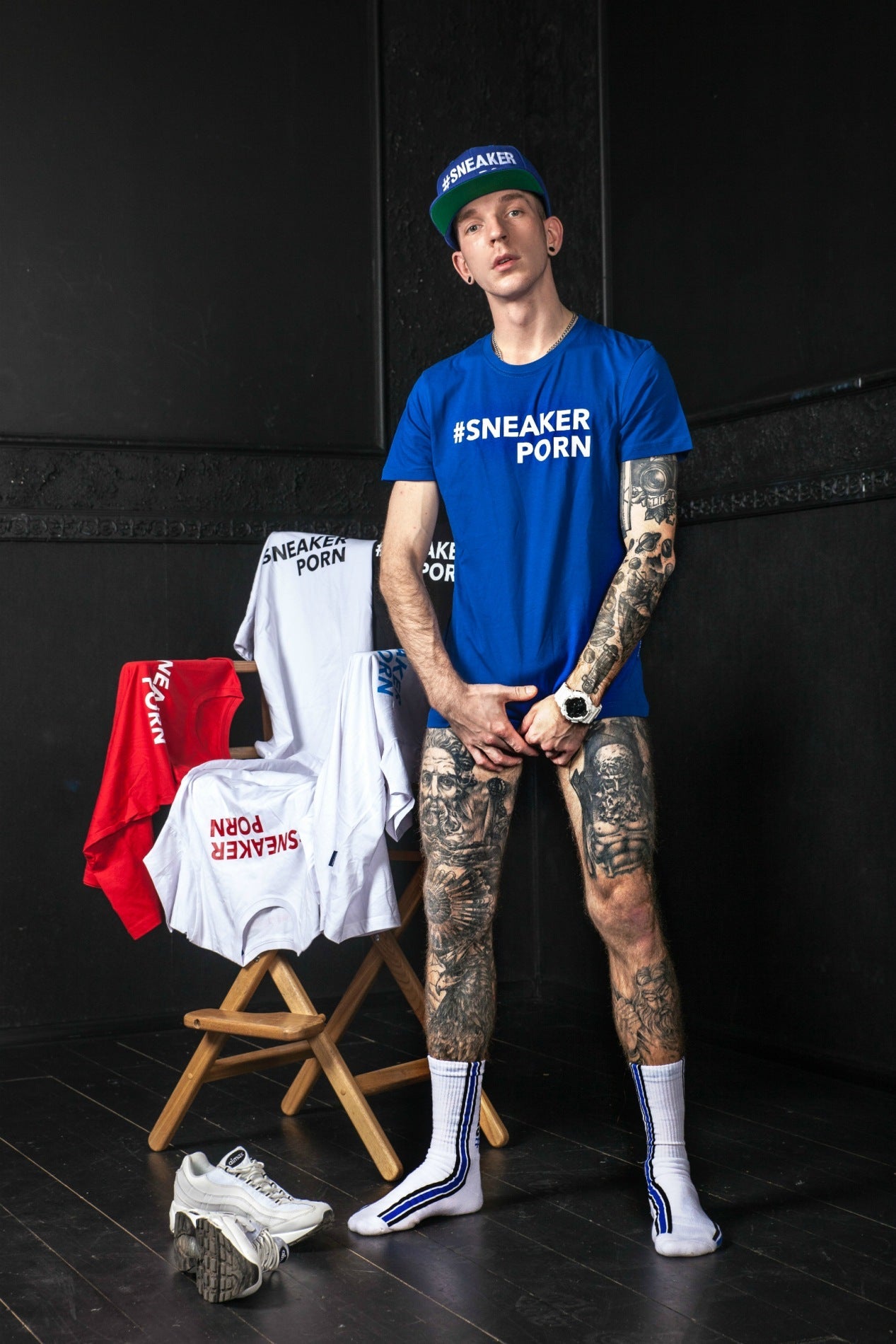 cooler junge mit tattoos auf den beinen und armen trägt ein blaues t-shirt und kappe mit sneakerporn aufschrift und die passenden socken in weiss und royalblau mit #sneakerporn von sk8erboy