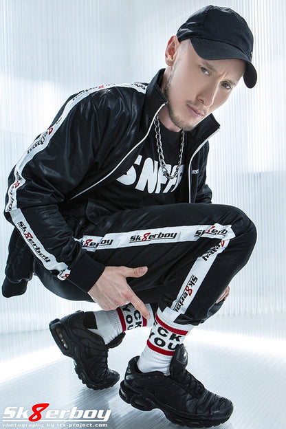 sexy gay in der hocke mit shiny Tracksuits von sk8erboy und basecap traegt fck you socken und schwarze nike tn sneaker