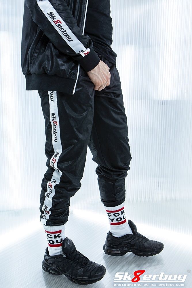 guy mit shiny pants und jacket von sk8erboy in schwarz und logo auf der seite traegt fck you socken und schwarze nike-tn sneaker zu seinem trainingsanzug