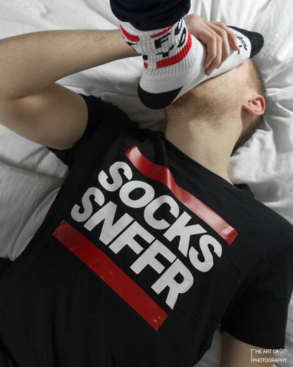 junge im bett mit schwarzen t-shirt von sk8erboy mit dem aufdruck socks snffr riecht an den socken von seinem freund der sk8erboy socken mit fck you traegt