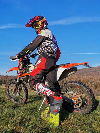 motor cross biker auf dem feld mit seinem motorrad zieht gerade die mx socks von sk8erboy aus seinen motorradstiefel in flecktarnmuster mit rot weiss schwarz und grau