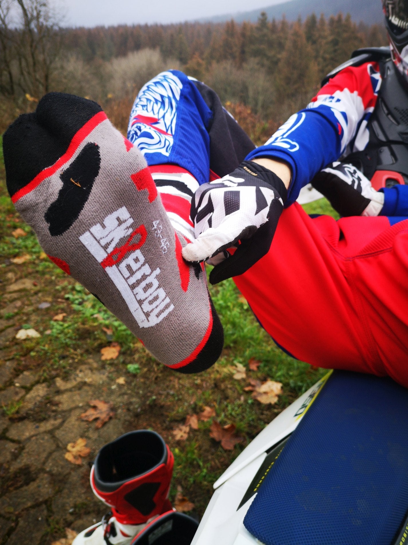 cross biker auf seinem motor cross bike mit mx socks von sk8erboy in flecktarn muster mit rot schwarz grauen flecken gegen lederflecken auf den socken