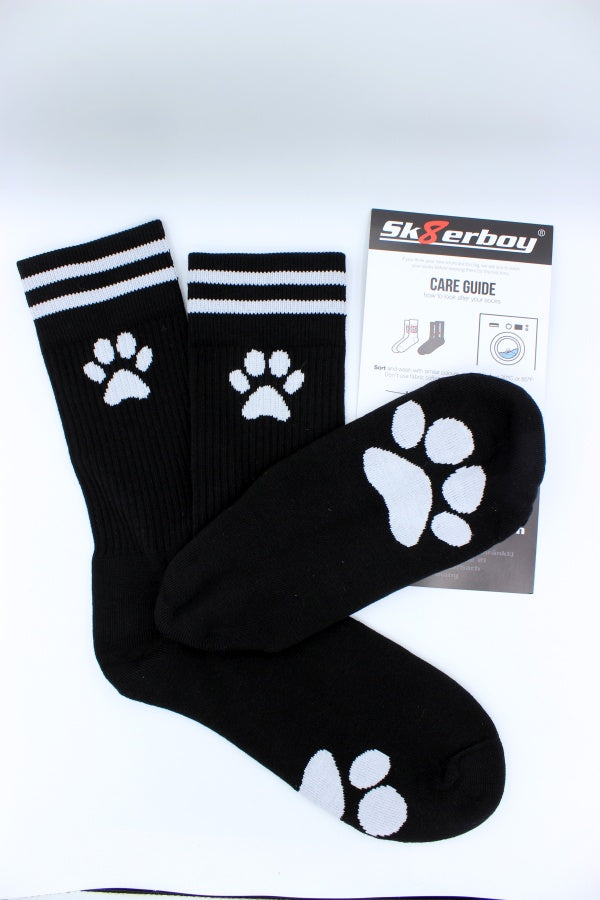 schwarze sk8erboy puppy socken mit weißer pfote an der seite und auf der sohle abgebildet mit verstecktem sk8erboy-logo auf der innenseite am bund mit verpackung und waschanleitung