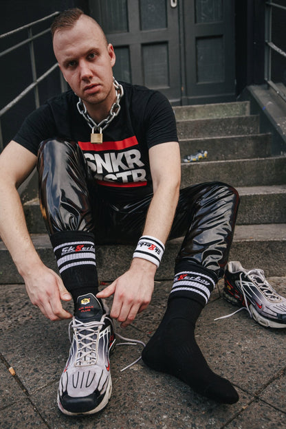 sk8erboy victory socken extra dünn in bekannter qualität jedoch besonders leicht und ideal für den sommer in schwarz von einem jungen gay mit pvc hose und fetisch t-shirt von sk8erboy getragen sitzt auf einer treppe